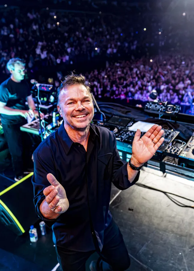Pete Tong smiling and gesturing to the crowd at an arena show